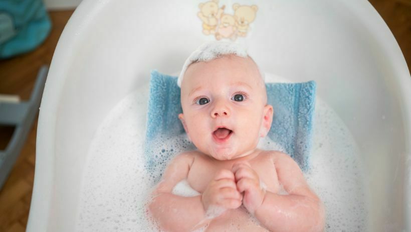 bebê sendo cuidadosamente banhado em uma banheira, com um adulto segurando-o com cuidado